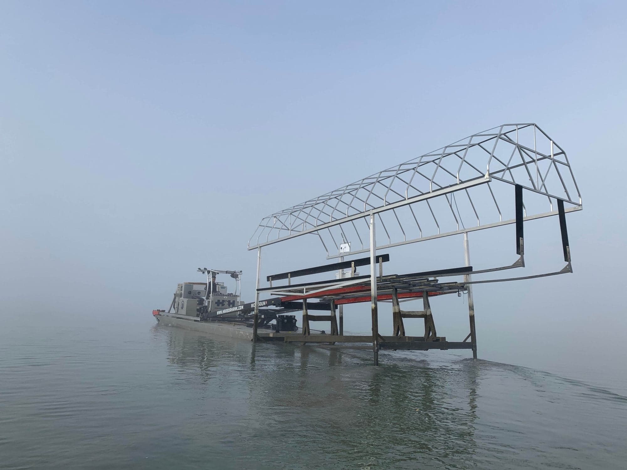 Boat lift with canopy frame being installed on a foggy morning